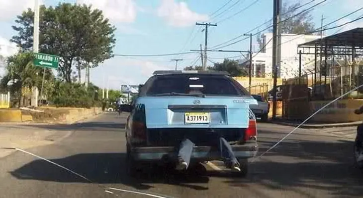 Los dominicanos somos así: hombre montado en el baúl de un carro